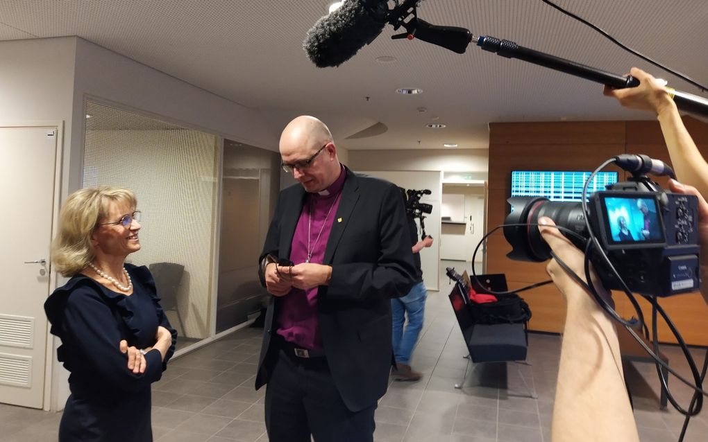 Vrouw in gesprek met veel langere man, terwijl een fotograaf op hen inzoomt