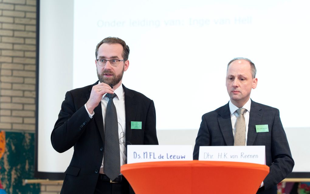 Twee mannen in pak staan voorin zaal.