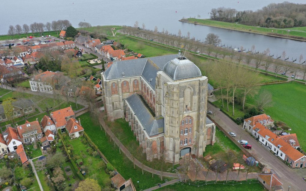 Een luchtfoto van een oude, grijze kerk met een stompe toren.