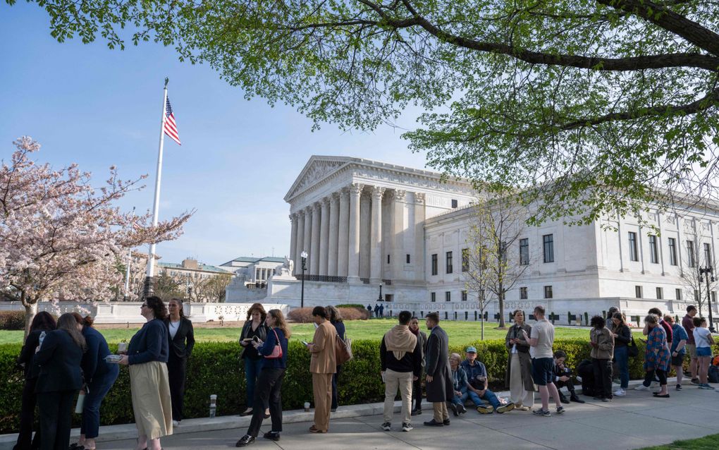 Mensen staan in een groene omgeving voor een witmarmeren gebouw dat lijkt op een Griekse tempel. 