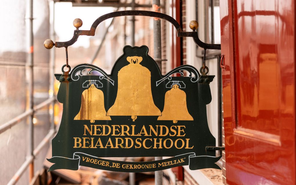Op donkergroen uithangbord staan drie goudkleurige klokken en de tekst ”Nederlandse Beiaardschool. Vroeger ”De gekroonde meelzak”.