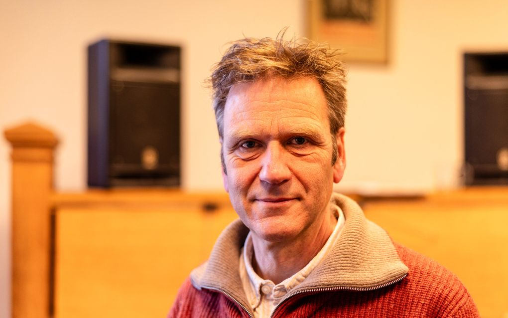 Een vijftiger, gekleed in een oranje vest, kijkt met een neutrale blik in de camera.