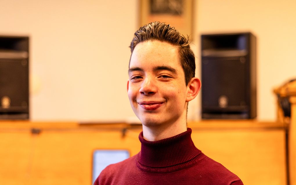 Een jongeman met een koltrui kijkt glimlachend in de camera.