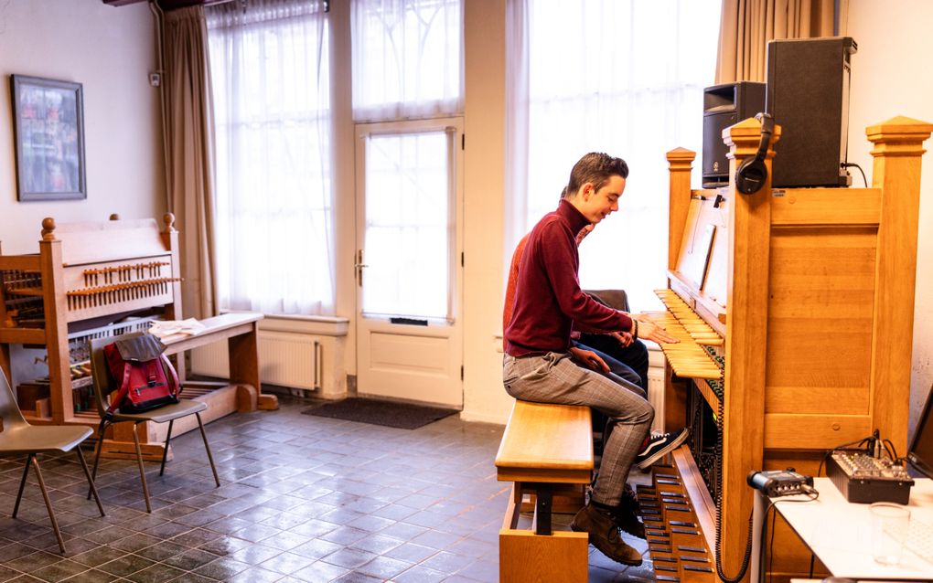 Een jongeman krijgt les op een oefenbeiaard. Zijn docent zit links van hem. Links in de ruimte staat een tweede oefenbeiaard.