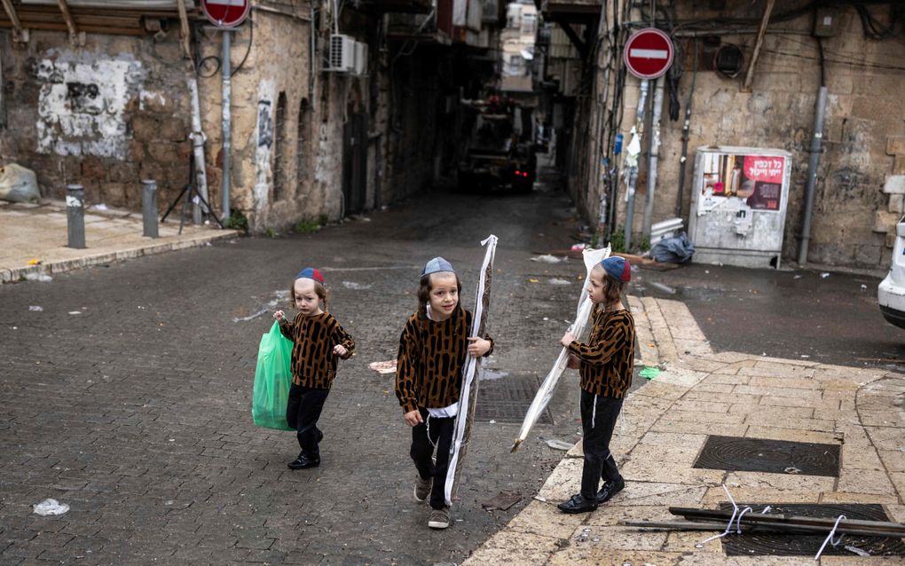 Jongens met keppeltjes op het hoofd dragen tassen bij zich in een grauwe straat