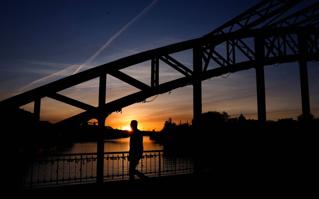 Een man wandelt over een brug in Parijs tijdens zonsopkomst.