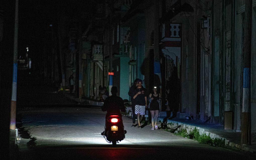 Een donkere straat waardoor een scooter rijdt. Aan de zijkant lopen enkele voetgangers.