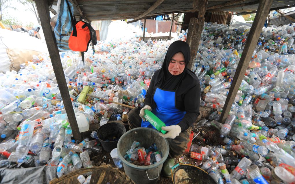 Een vrouw zit tussen bergen plastic flessen om deze te sorteren.