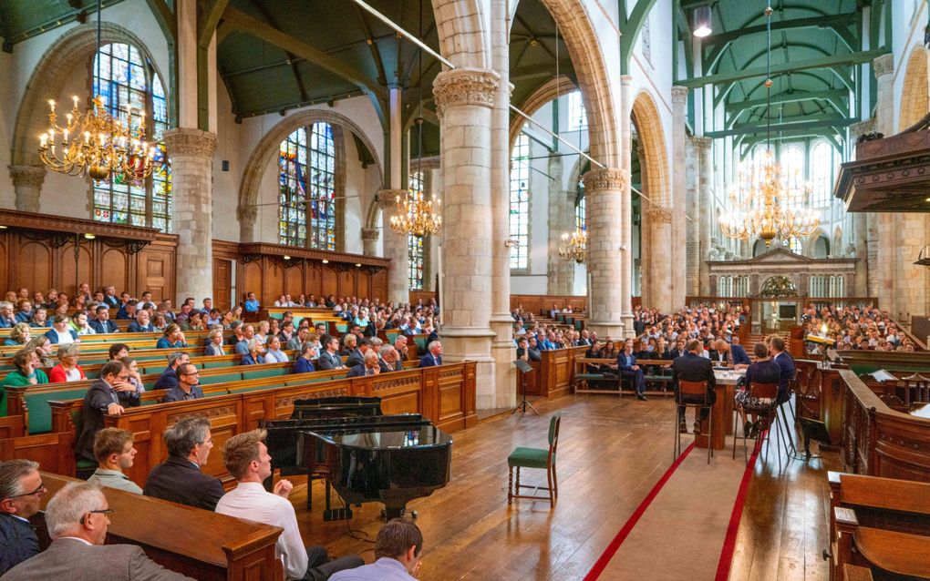 Oude kerk met groen plafond, gouden kroonluchters, banken met houtsnijwerk en grote houten kansel. In het midden van de kerk staat een zwarte vleugel