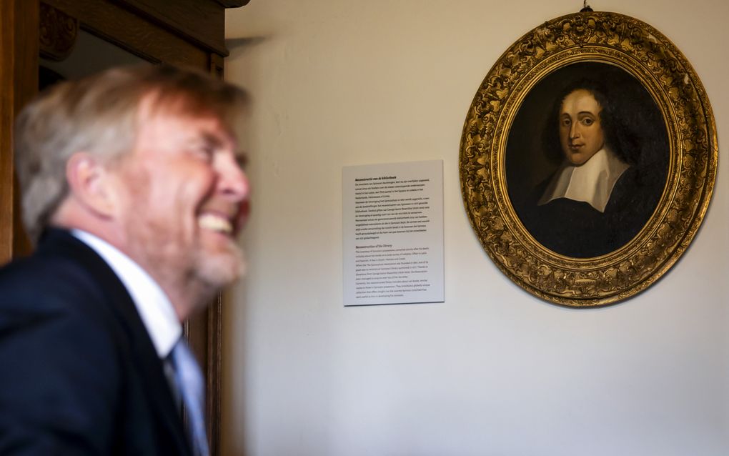 Een lachende koning bij een portret van Baruch Spinoza.