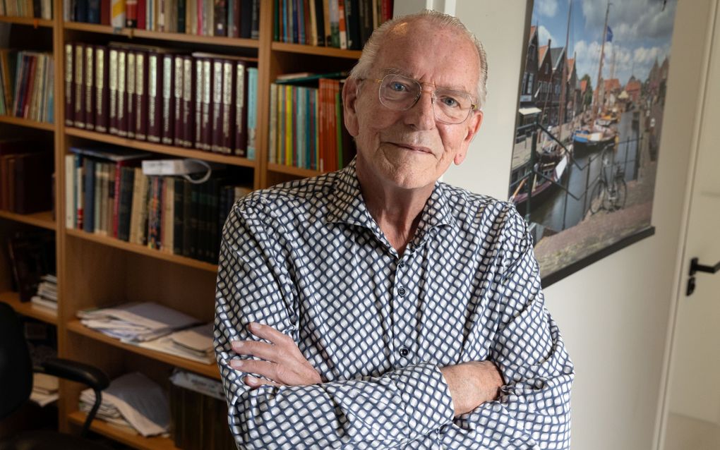 Dominee Van de Groep, een man met grijs haar, bril op, zwart-wit overhemd aan, voor een boekenkast.