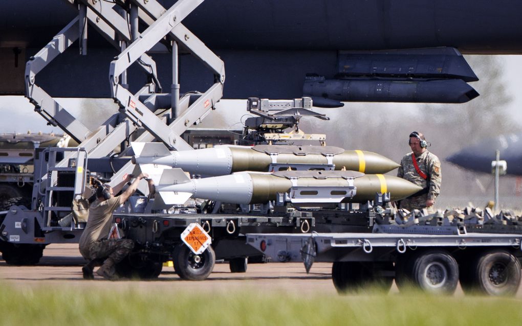 Man staat naast vrachtwagen waarop bommen liggen die onder vliegtuig worden gehangen.