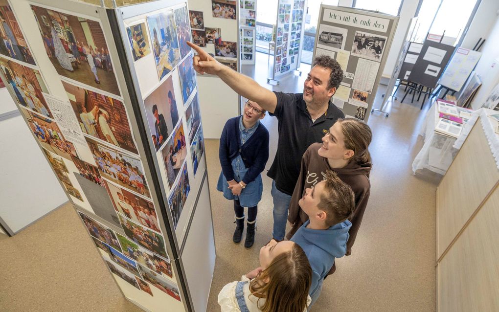 Een meester wijst een aantal leerlingen iets aan op een fotozuil. 