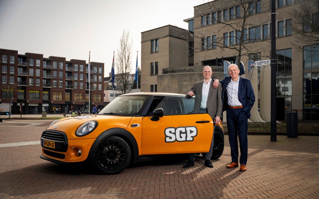 Twee mannen staan bij een oranje auto met SGP-bestickering.