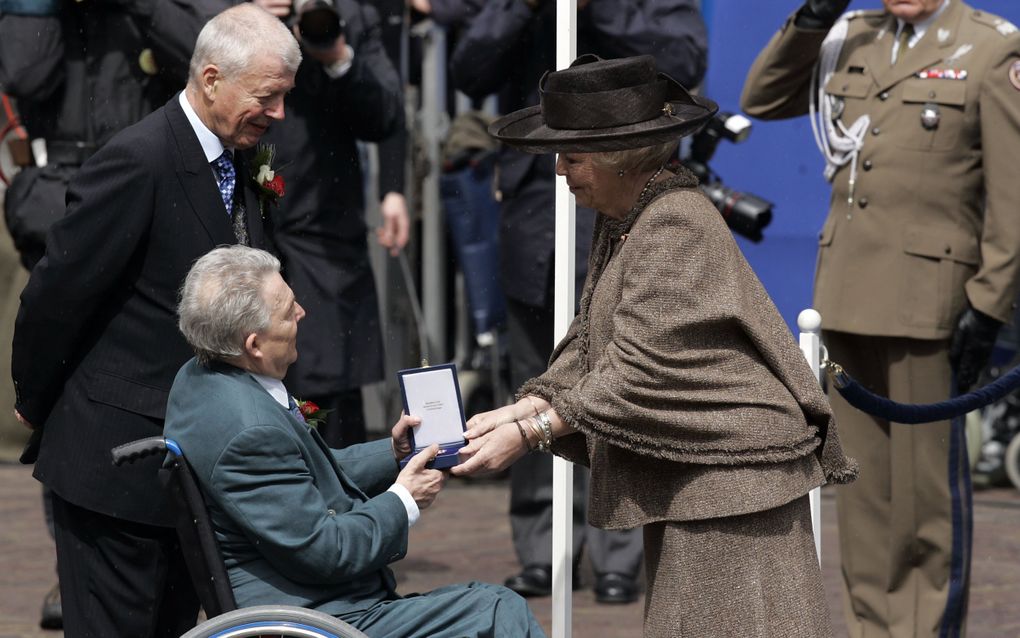 Een vrouw met een hoed overhandigt een doosje aan een man in een rolstoel.