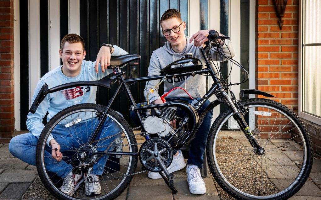 Twee jongens zitten lachend achter een zogeheten briets, een kruising tussen een brommer en een fiets.