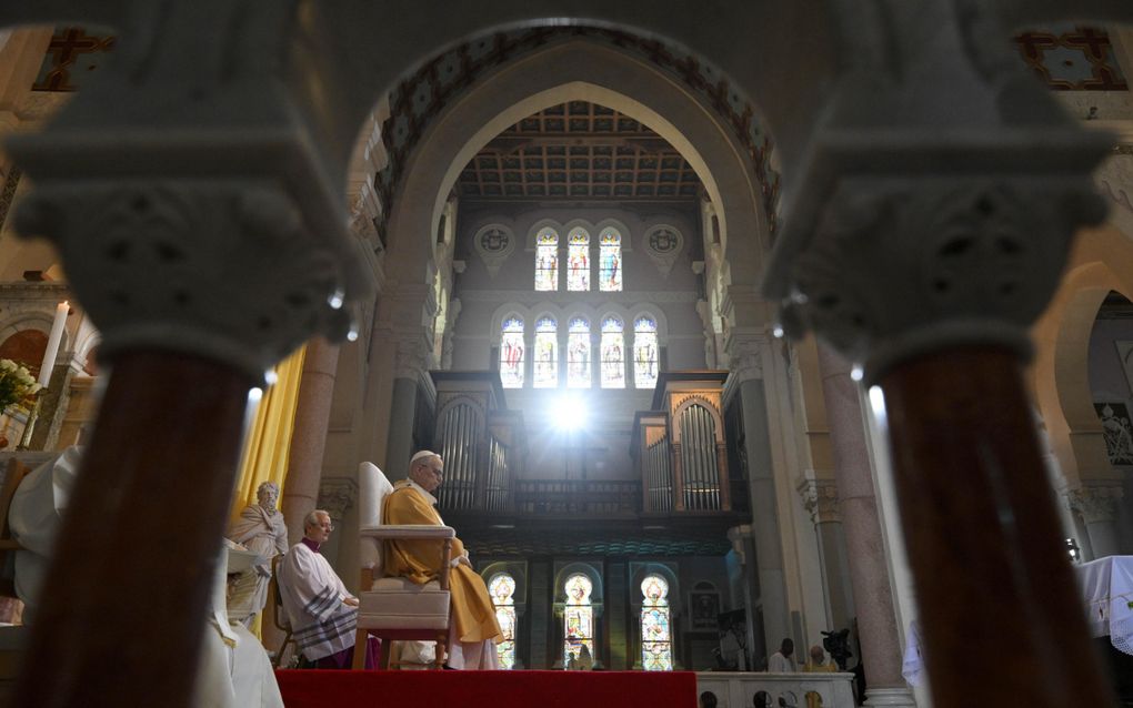 Paus Leo, in gele mantel, zit op een stoel in een kerk.