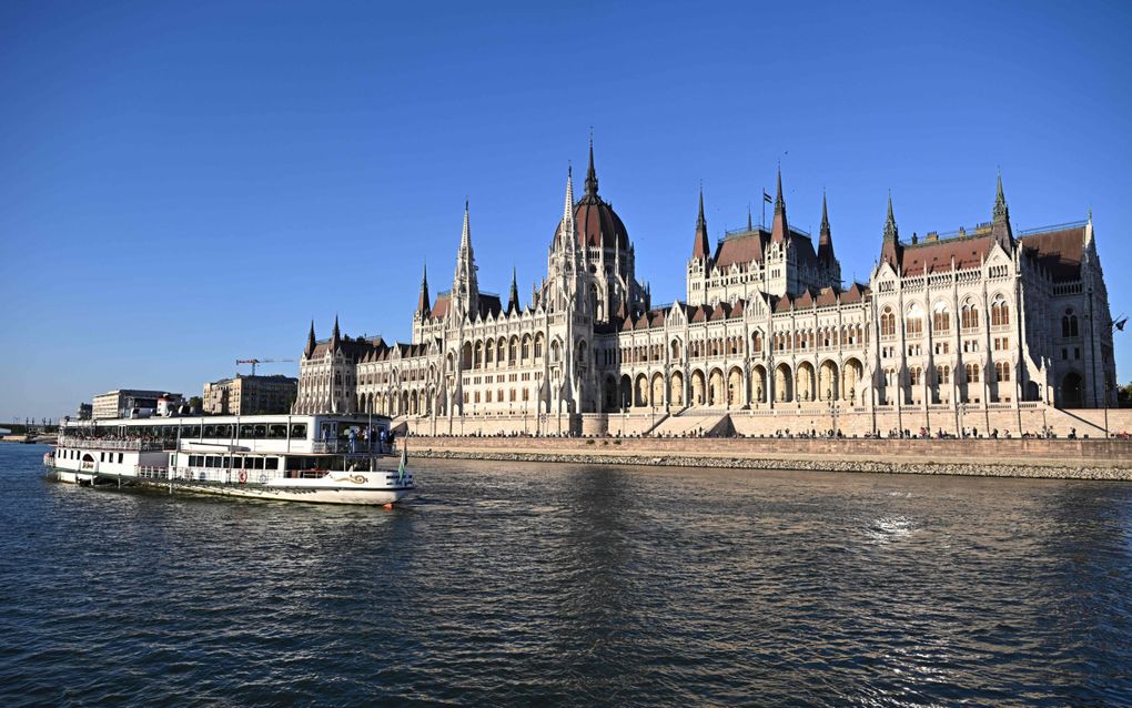 Een groot gebouw steekt af tegen de blauwe lucht. Een rondvaartboot vaart voorbij.
