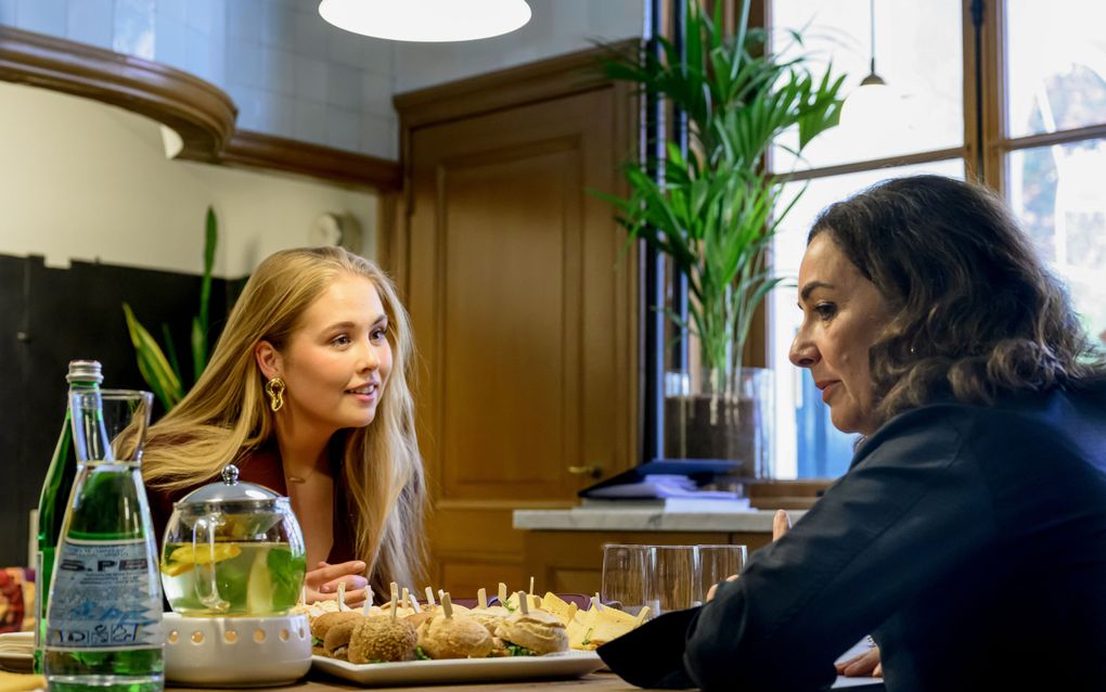 Twee vrouwen zitten aan een tafel waarop broodjes staan, een kan water en een pot thee.
