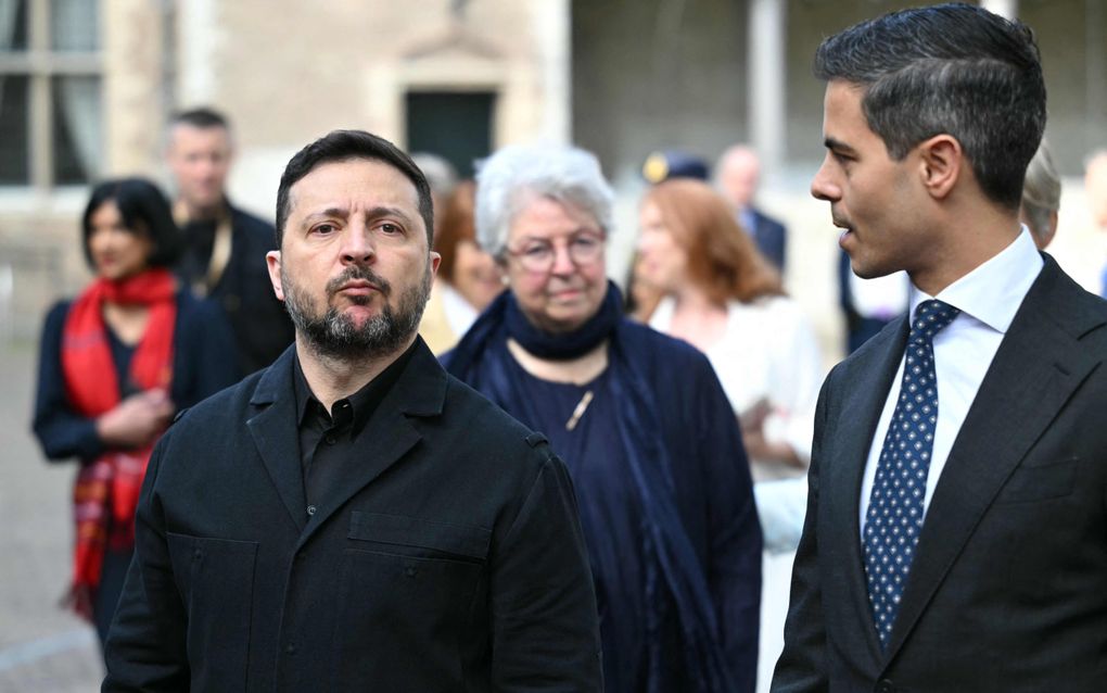 Een man in pak praat tegen een man in zwarte kleding.