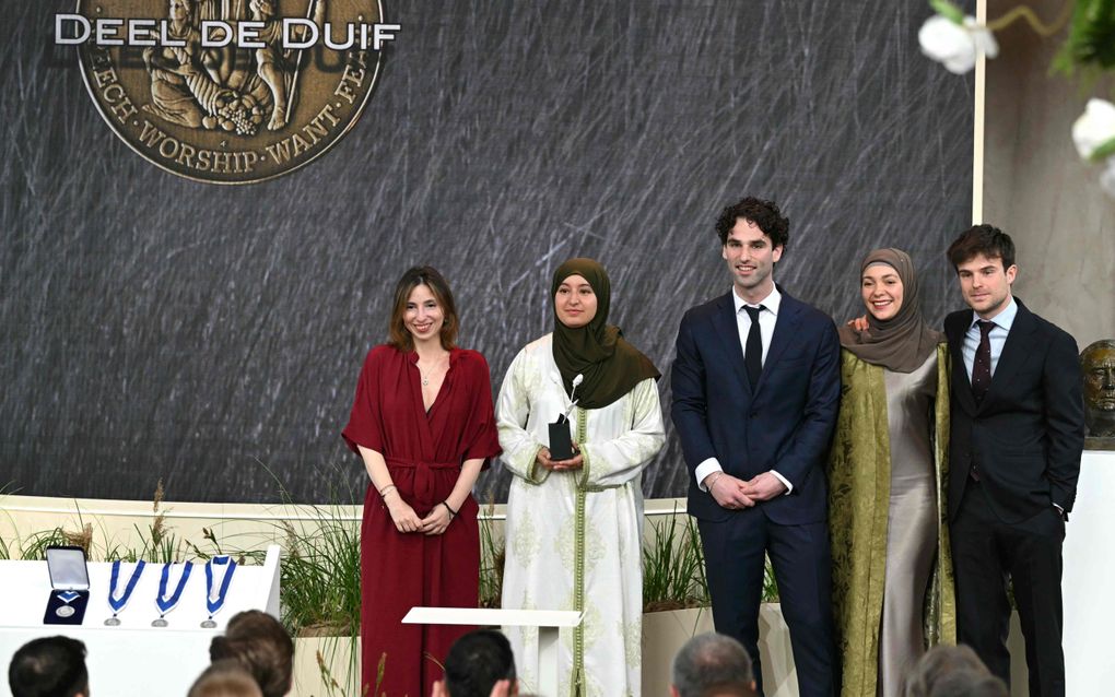 Vijf jongeren op een rij. Een man slaat zijn arm om de schouder van een vrouw met hoofddoek.