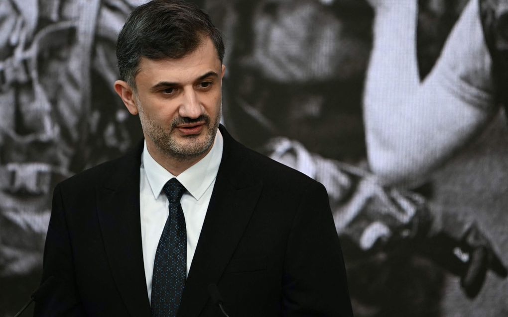 Een man in donker pak en met baardje spreekt.