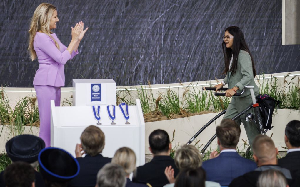 Vrouw in paars kleding applaudisseert voor jonge vrouw met loopondersteuning.