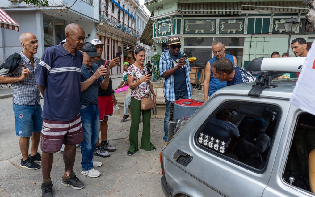Mensen bekijken en filmen een auto die een grote pot met houtskoolgas achterop heeft staan.&nbsp;