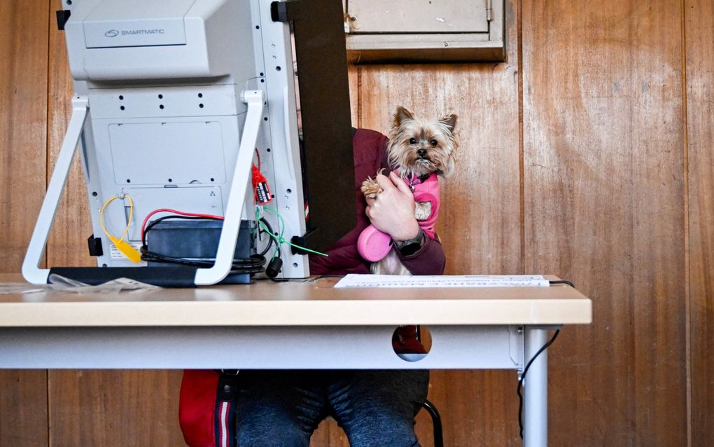 Een grote machine waar een vrouw achter verdwijnt. Haar hond met roze jasje is nog wel zichtbaar