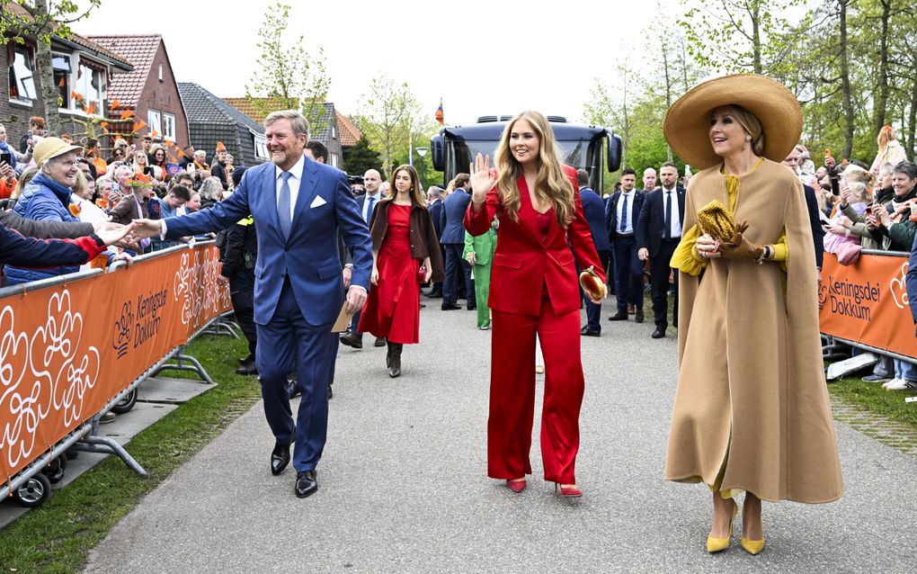 Leden van de koninklijke familie lopen over een pad. Links en rechts staan mensen achter dranghekken. De koning geef mensen een hand en Amalia zwaait. Op de voorgrond loopt de koningin, op de achtergrond prinses Alexia en mannen in donkere pakken.