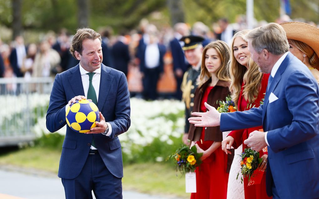 Een man in een blauw pak met groene stropdas houdt een geel-blauwe bal vast. Rechts prinses Alexia, prinses Amalia, de koning en de koningin.