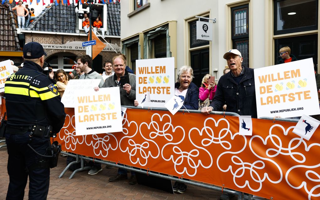 Achter dranghekken staan enkele mensen. Ze hebben borden vast waarop staat: „Willem de laatste”, met emoticons van zwaaiende handjes. Ze hebben ook vlaggetjes vast met een zwarte dinosaurus met een kroontje op.