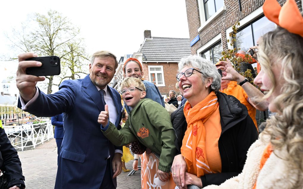 Een jongetje met blond haar en bril steekt zijn duim op, terwijl de koning een selfie met hem maakt.