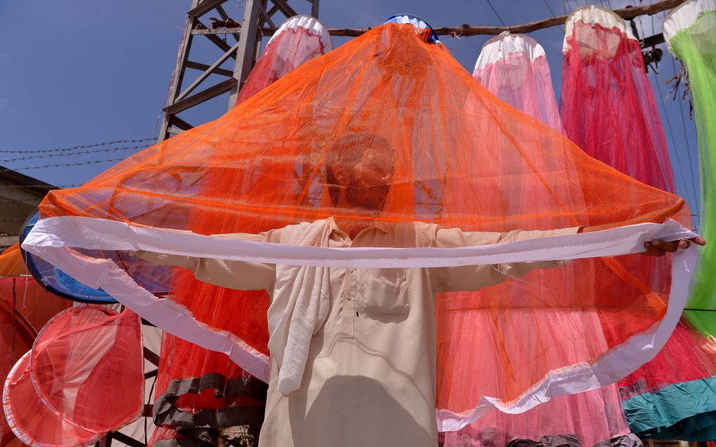Een in het beige geklede Pakistaanse verkoper laat een oranje muskietennet zien.