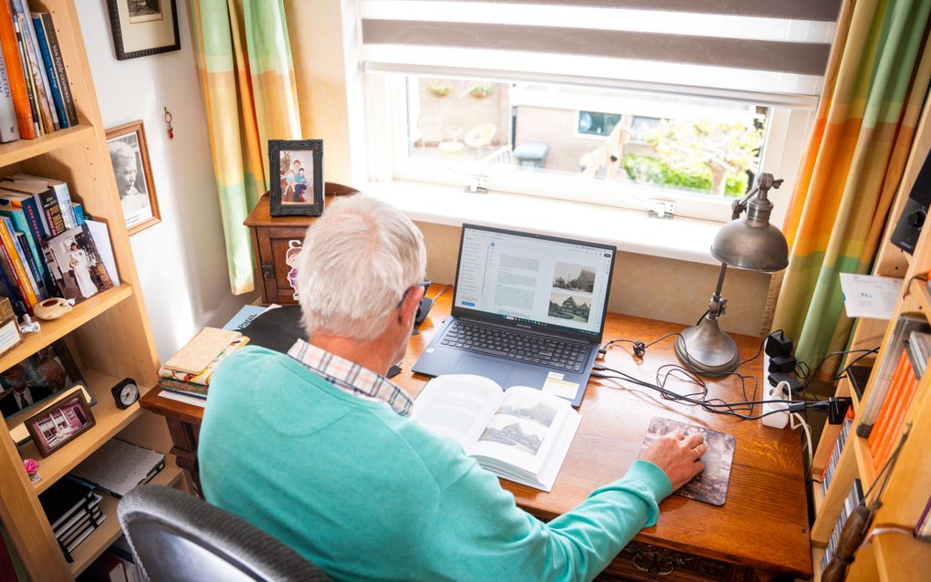 Man in azuurblauwe trui zit aan een bureau op een laptop te werken.