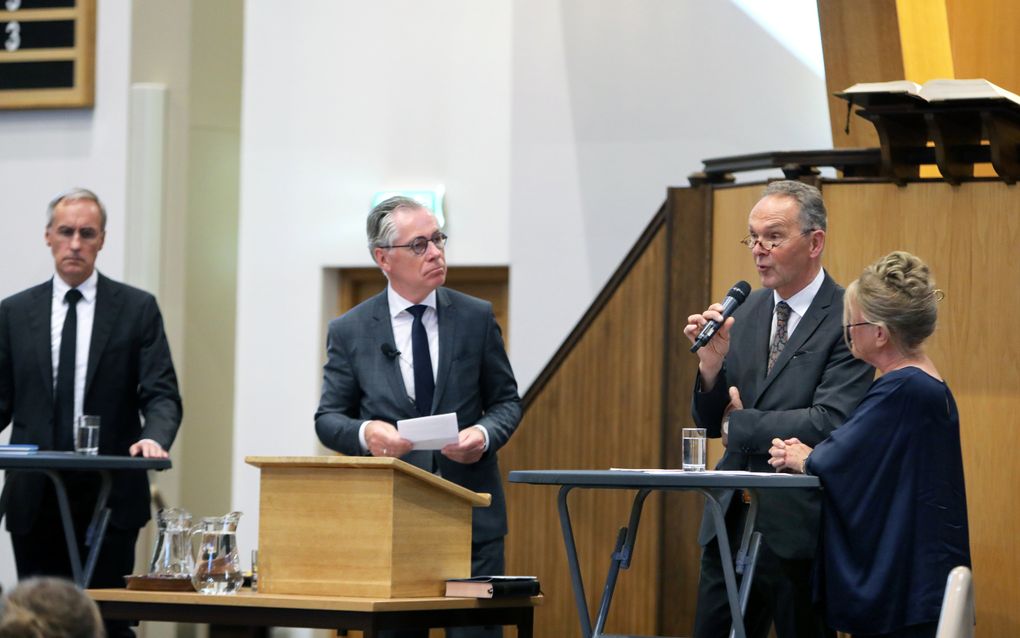 Drie mannen en een vrouw staan achter een statafel of een lessenaar.