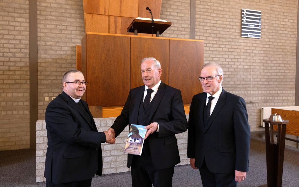 J. van den Ende (m.) biedt het boek “Mfundisi Tallach, een man met een brandend hart voor zielen” aan ds. Bruce Jardine (l.) aan. Het boek wordt tijdens de Mbuma zendingsdag officieel gepresenteerd. Rechts ouderling Robert Dickie. beeld Dirk Hol 