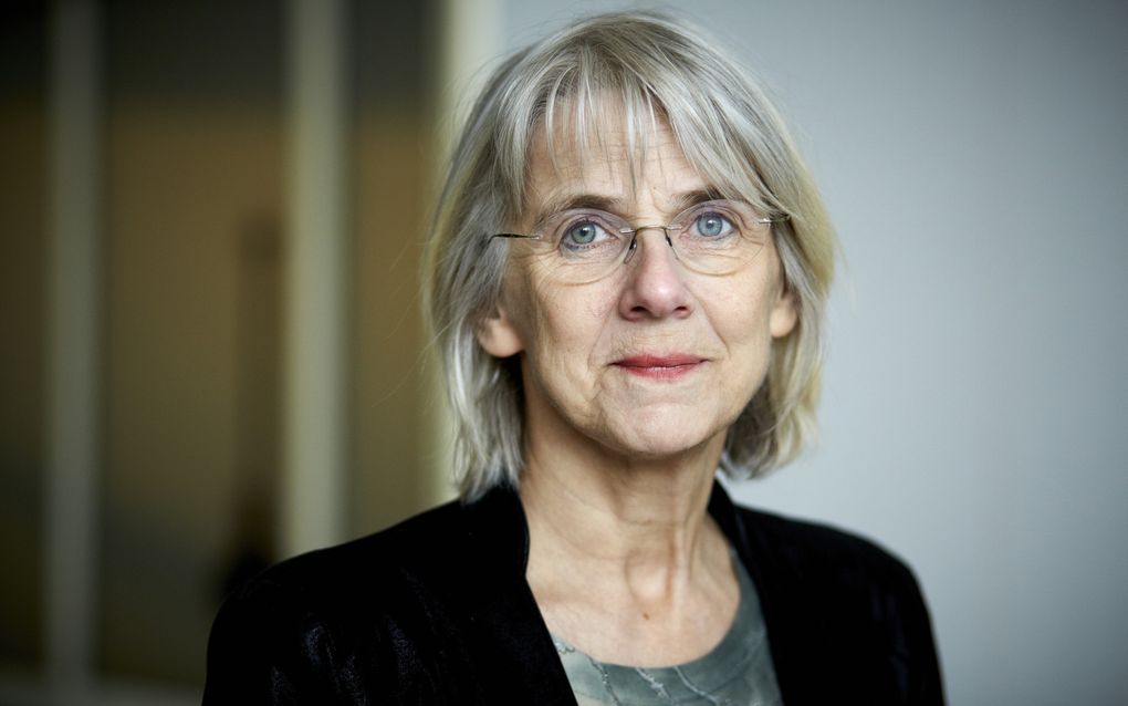 Oudere vrouw met halflang grijs haar en lichte bril. Ze draagt een zwart jasje.