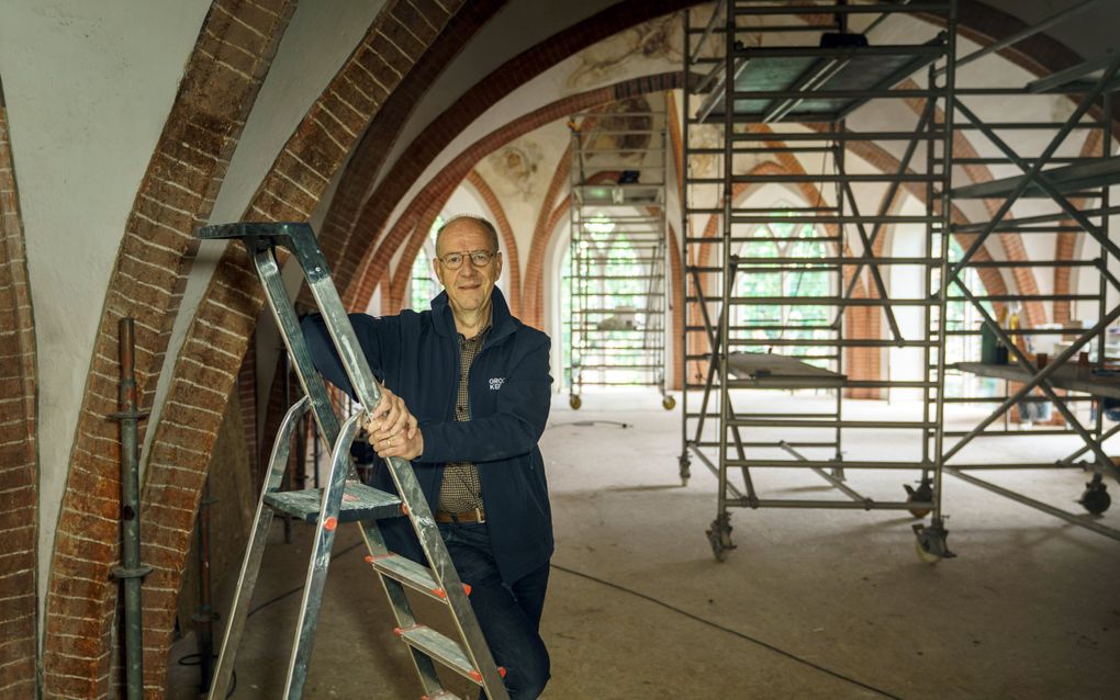 Een oudere man, op een trapje in een kerk. De kerk staat vol steigers.