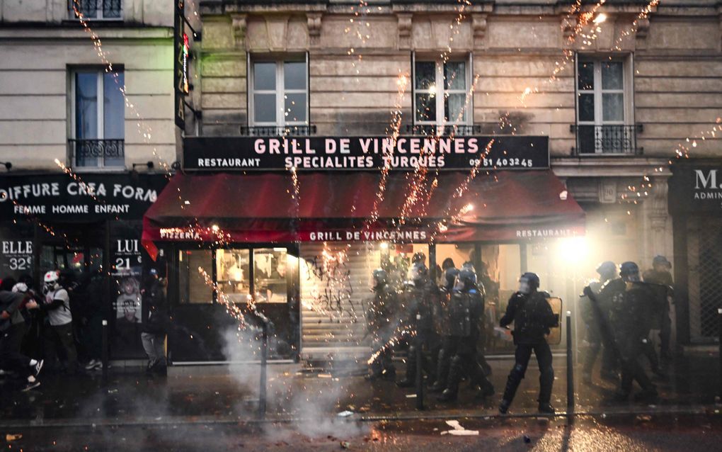 Een Frans restaurant met op de voorgrond politie met helmen en wapens. Vuurwerk vliegt door de lucht. 