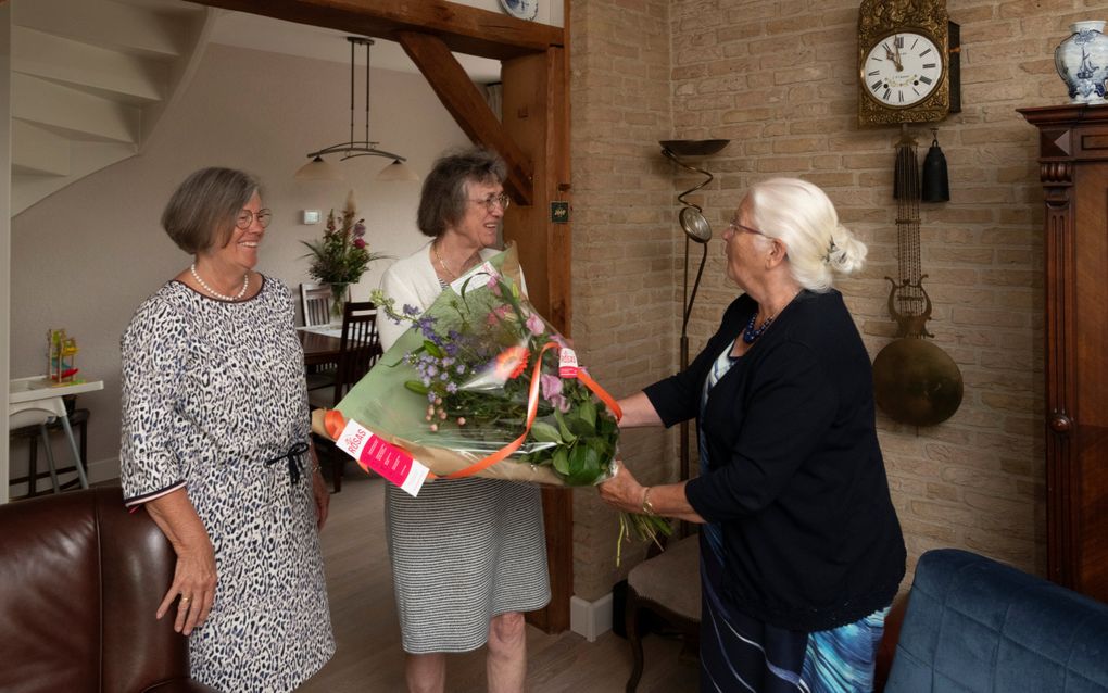 Janna Pluimers (rechts) geeft Diny Scheppink (in het midden) een bloemetje. Diny Pluimers kijkt toe. Ruben Meijerink