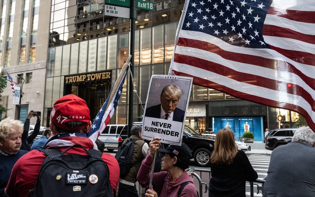 Aanhangers van Donald Trump spreken bij de Trump Tower in New York hun steun uit voor de veroordeelde oud-president. Een man houdt een bord omhoog waarop hij Trump oproept om nooit op te geven. beeld AFP, Stephanie Keith