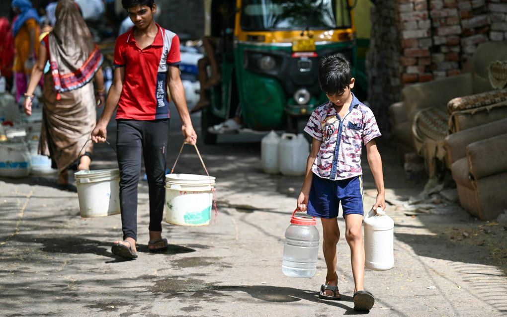 Kinderen dragen emmers en flessen met water, geleverd door een gemeentelijke tanker in New Delhi. In de stad steeg het kwik deze week tot 52,3 gracen Celcius. beeld AFP, Money Sharma