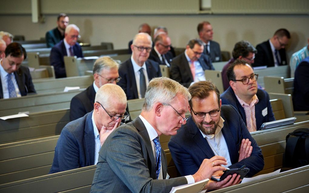 Afgevaardigden in de kerkbanken in Rijnsburg. Ds. M. Groen (l.) toont iets op zijn telefoon aan ds. R.G. den Hertog. beeld Fred Libochant Fotografie