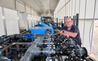 Een man met bril leunt op een installatie met allerlei buizen en slangen. 