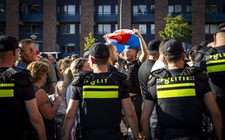Een groep mensen demonstreert met onder andere een Nederlandse vlag met op de voorgrond politieagenten.