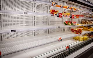 Lege witte schappen in het koelvak van een supermarkt. Hier en daar ligt nog wat fruit. 