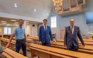 Drie mannen, twee in pak met stropdas, en een, de linkse, casual. Ze staan in de kerk, verderop is het orgel te zien.
