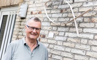 Man met bril voor zijn huis waar naast de voordeur een metalen ichthusteken hangt.