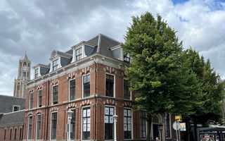 Oud gebouw met hoge ramen, met op de achtergrond een gotische kerktoren.